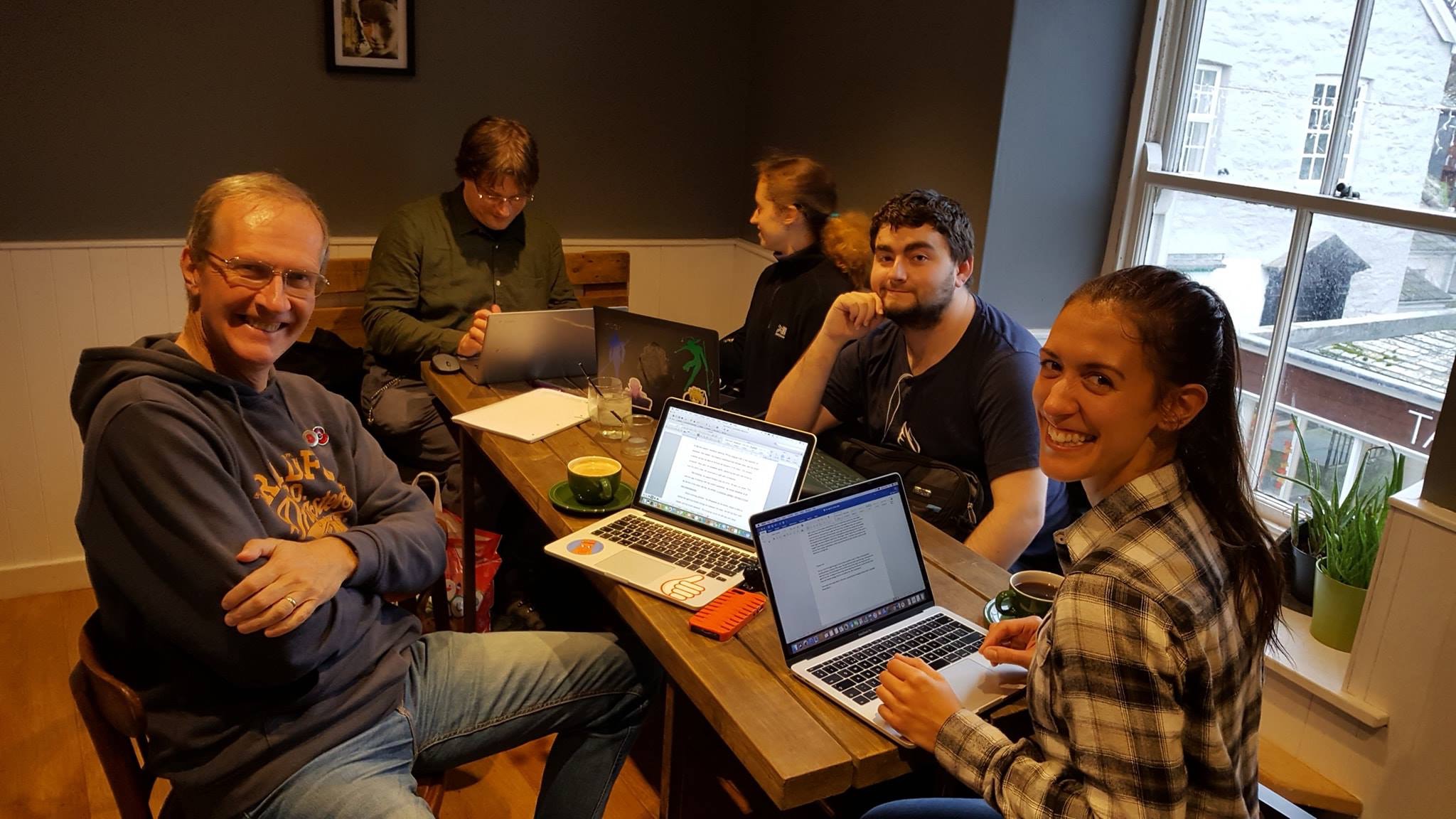 Writers from the Cornwall Wrimos sitting around a table in a coffee shop with laptops and coffee